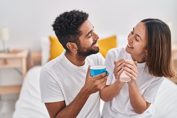 Man and woman couple hugging each other drinking coffee at bedroom