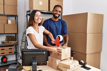 Man and woman business partners packing package using tape at storehouse