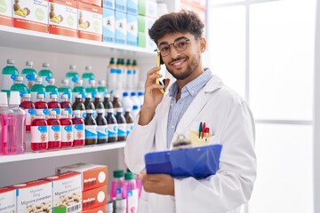 Young arab man pharmacist talking on smartphone reading document at pharmacy