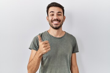 Young hispanic man with beard wearing casual t shirt over white background doing happy thumbs up gesture with hand. approving expression looking at the camera showing success.