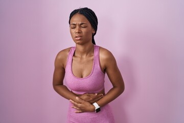 African american woman with braids wearing sportswear over pink background with hand on stomach because indigestion, painful illness feeling unwell. ache concept.