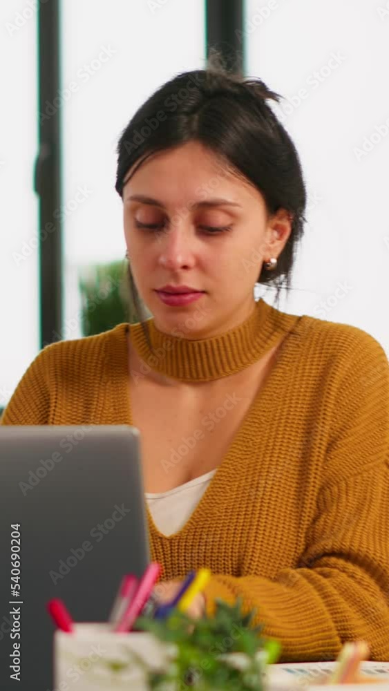 Poster cheerful business lady typing on laptop computer and smiling sitting at desk in busy start up office