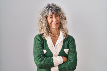 Middle age woman standing over white background winking looking at the camera with sexy expression,...