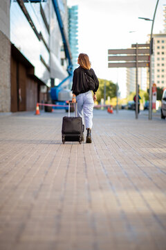 behind travel woman pulling suitcase on sidewalk