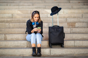 Full length woman sitting on stairs with suitcase and mobile phone