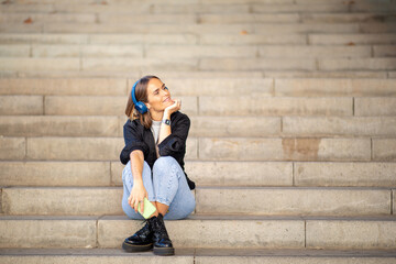 woman sitting on stairs listening to music with smart phone and headphones