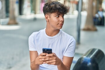 Young hispanic teenager using smartphone with relaxed expression at street