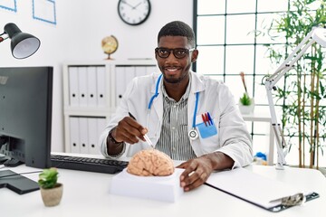 Young african american man wearing neurologist uniform holding brain at clinic