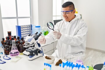 Young latin man scientist looking cannabis herb with loupe at laboratory