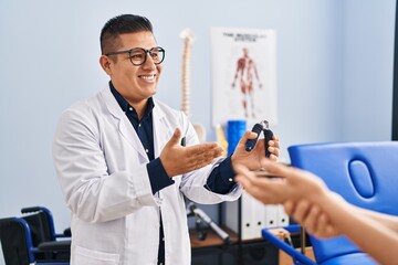 Young latin man pysiotherapist explaining hand press machine to patient at rehab clinic