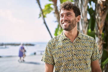 Young hispanic man smiling confident walking at seaside