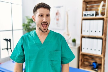 Young physiotherapist man working at pain recovery clinic angry and mad screaming frustrated and furious, shouting with anger. rage and aggressive concept.