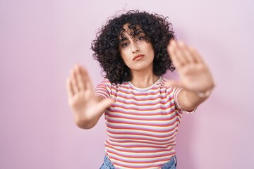 Young middle east woman standing over pink background doing frame using hands palms and fingers, camera perspective