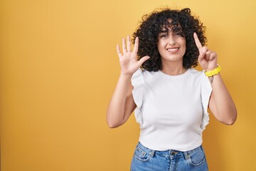Young middle east woman standing over yellow background showing and pointing up with fingers number six while smiling confident and happy.