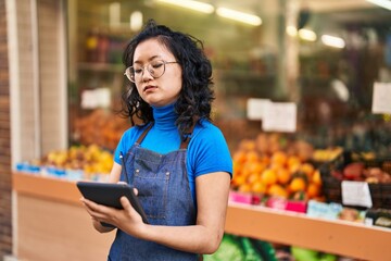 Young chinese woman employee using touchpad at fruit store