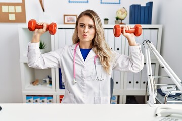 Young beautiful doctor woman holding dumbbells for sport therapy looking at the camera blowing a kiss being lovely and sexy. love expression.