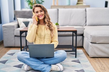 Young woman using laptop and talking on smartphone at home