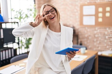 Young caucasian woman working at the office wearing glasses doing peace symbol with fingers over face, smiling cheerful showing victory