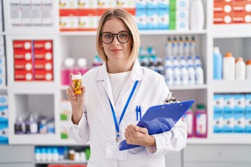 Young caucasian woman working at pharmacy drugstore holding pills relaxed with serious expression on face. simple and natural looking at the camera.