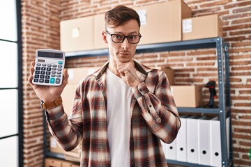 Caucasian business man working at small business ecommerce holding calculator serious face thinking...