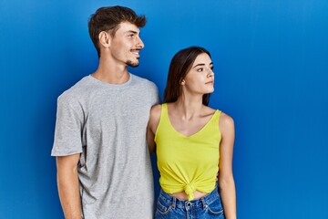 Fototapeta premium Young hispanic couple standing together over blue background looking to side, relax profile pose with natural face and confident smile.