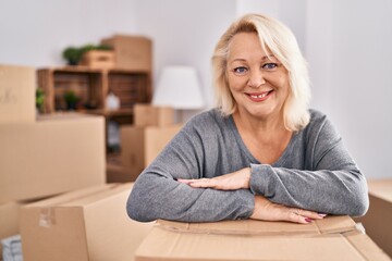 Obraz premium Middle age blonde woman smiling confident leaning on package at new home