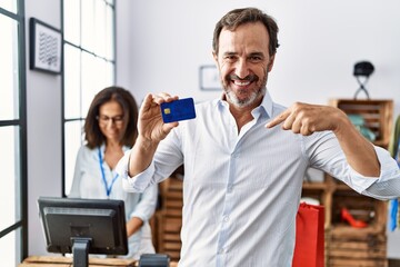 Hispanic man holding credit card at retail shop pointing finger to one self smiling happy and proud