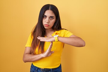 Young arab woman standing over yellow background doing time out gesture with hands, frustrated and serious face