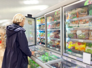  Man choosing frozen food from a supermarket freezer., reading product information