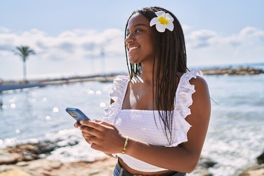 Young african american girl smiling happy using smartphone at the beach - Powered by Adobe