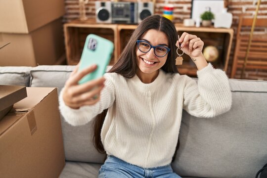 Young hispanic woman smiling confident make selfie by the smartphone holding key of new house at new home