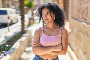 Young hispanic woman standing with arms crossed gesture and relaxed expression at street