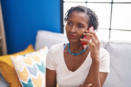 Middle age african american woman talking on smartphone with worried expression at home