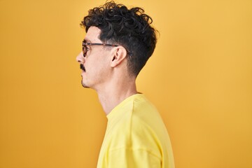 Obraz premium Hispanic man wearing glasses standing over yellow background looking to side, relax profile pose with natural face with confident smile.