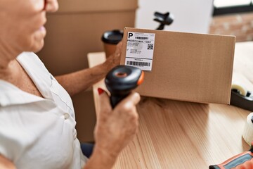 Senior grey-haired woman business worker scanning package label at office