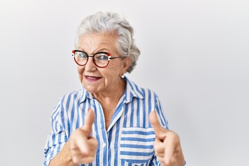 Senior woman with grey hair standing over white background pointing fingers to camera with happy and funny face. good energy and vibes.