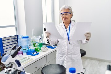 Senior grey-haired woman wearing scientist uniform reading document at laboratory