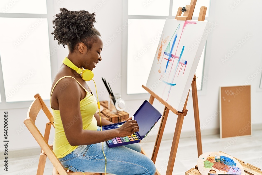 Poster Young african american artist woman using headphones drawing at art studio.