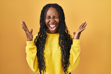 African woman standing over yellow background celebrating mad and crazy for success with arms...