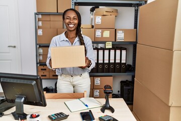 African woman working at small business ecommerce holding box winking looking at the camera with sexy expression, cheerful and happy face.