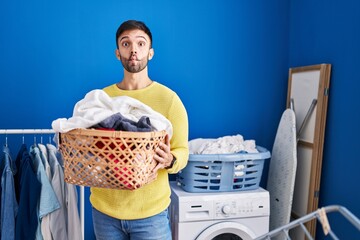 Hispanic man holding laundry basket making fish face with mouth and squinting eyes, crazy and...