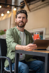 Young bearded man sitting in the cafe and having a break in work