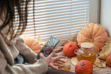 Girl taking photo of pumpkins, autumn leaves and teapot on a window. Girl photographing on phone rustic halloween composition. Happy Thanksgiving and Halloween