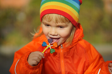 Portrait of a cute little girl holding a large rainbow lollipop. The baby eats a sweet, big lollipop.