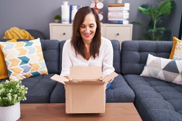 Middle age brunette woman opening cardboard box smiling with a happy and cool smile on face....