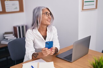 Middle age grey-haired woman business worker using laptop and smartphone at office