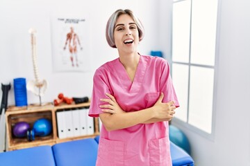 Young nurse woman working at pain recovery clinic happy face smiling with crossed arms looking at the camera. positive person.