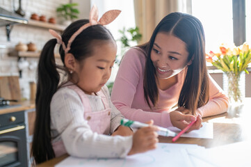 Young mother watching her daughter drawing with a colored marker
