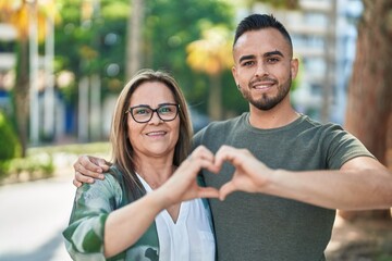 Naklejka premium Man and woman mother and daugther doing heart gesture with hands at park