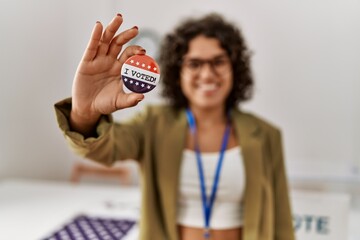 Young hispanic woman smiling confident holding i voted badge at electoral college